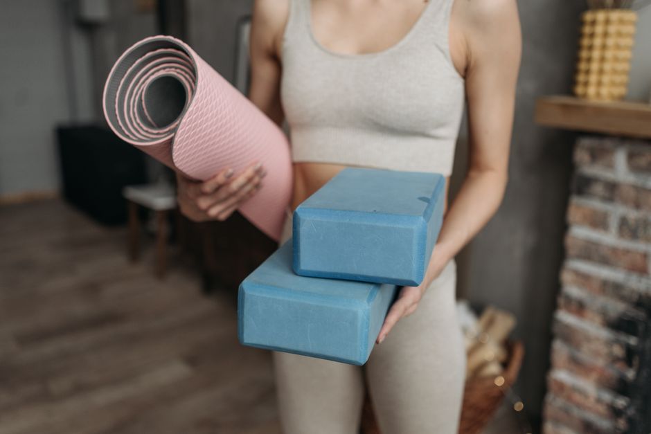 Woman holds yoga mat and blocks indoors, highlighting fitness routine at home with modern active wear.